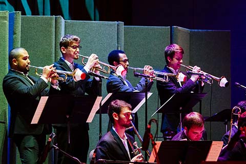 Brass players dressed in dark suits perform on stage